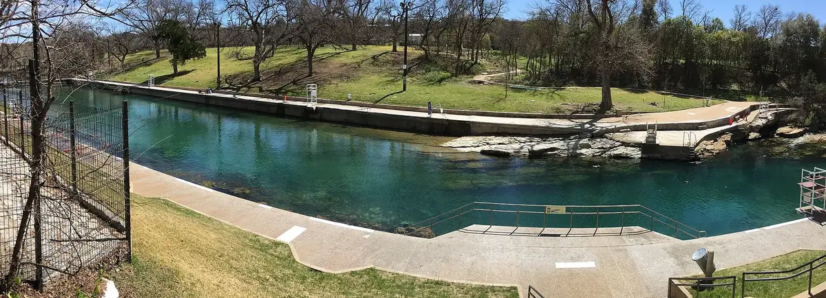 The clear green water of Barton Springs Pool in Austin with the lawn and trees along its bank