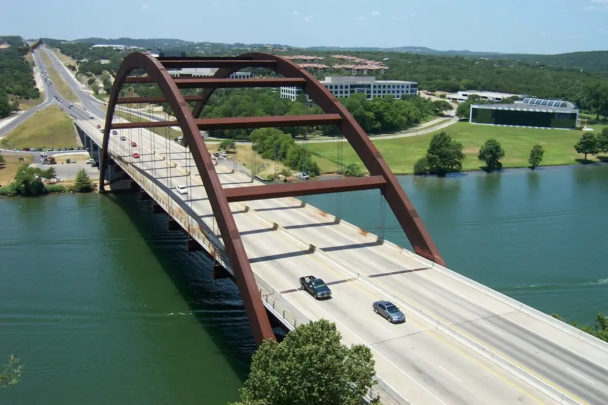 The rust red arch of the Pennybacker Bridge over Lake Austin with the Hill Country behind it
