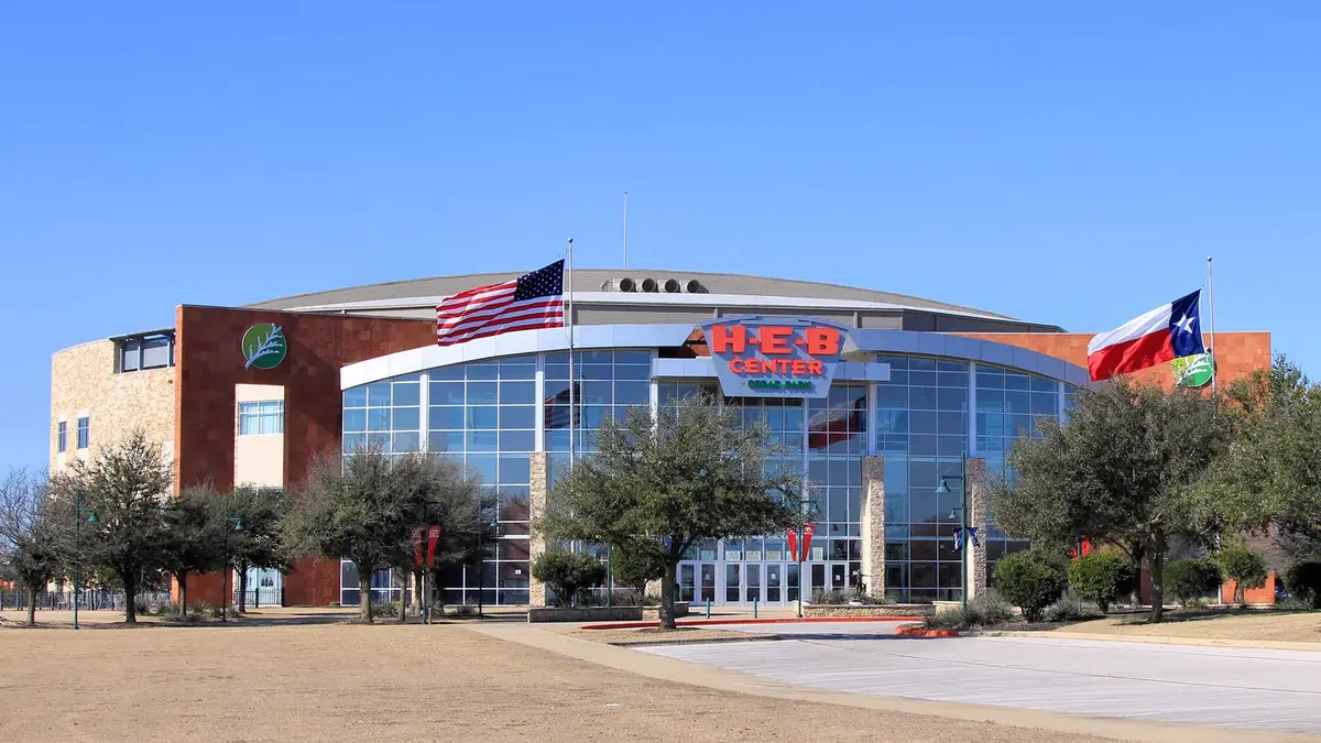 The glass front of the H-E-B Center arena in Cedar Park with the US and Texas flags out front