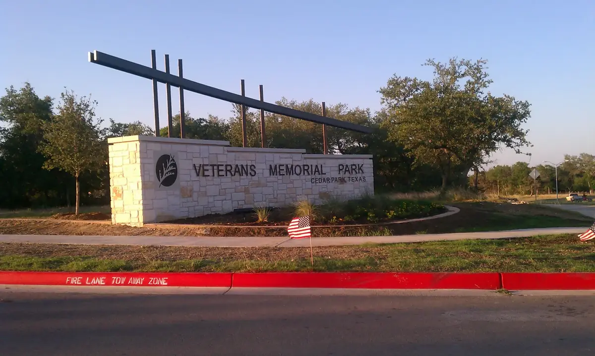 The limestone Veterans Memorial Park sign in Cedar Park with a steel sculpture and trees behind it