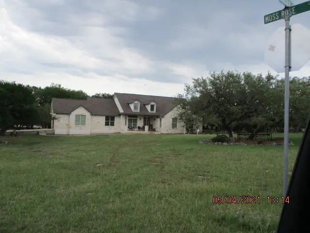 Single-story ranch home on open acreage seen from the road with a street sign
