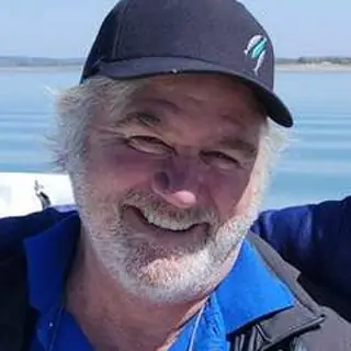 Frank Hargis, owner of Ruddy's Roofing, smiling in a navy cap on the lake