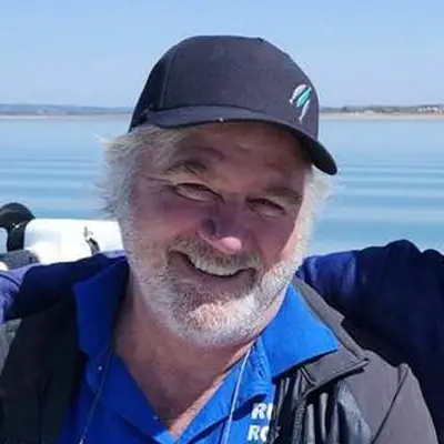 Frank Hargis in a navy cap and blue jacket, smiling on a boat with the lake behind him