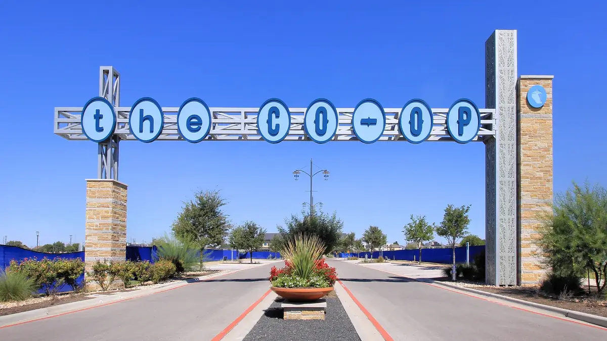 The Co-op District gateway sign over the entry road in Hutto under a clear blue sky