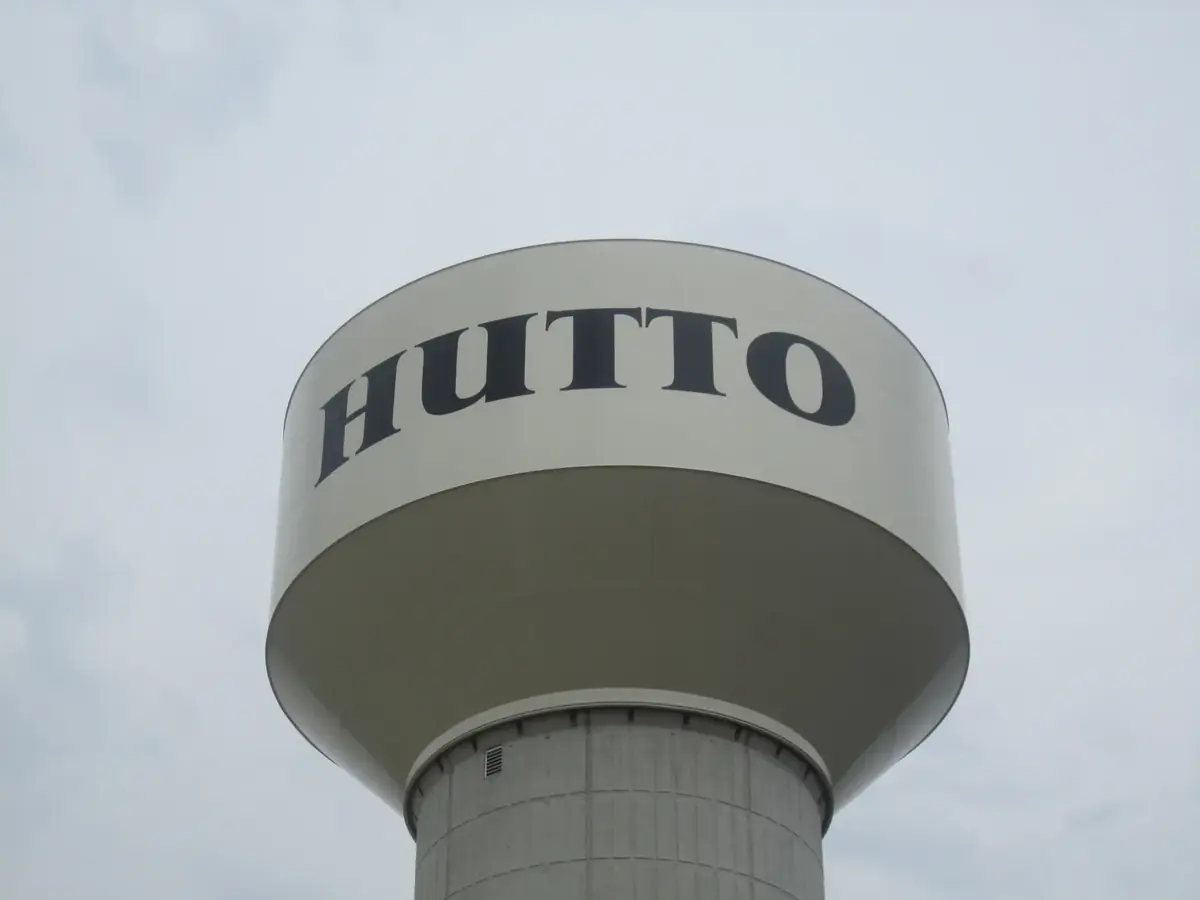 The Hutto water tower with HUTTO painted on the tank against a gray sky