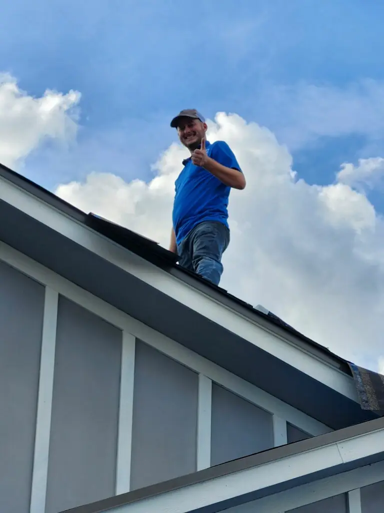 Jake Ruddy on a roof edge giving a thumbs up against a blue sky