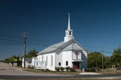 The white wooden Leander Presbyterian Church and its steeple under a deep blue sky