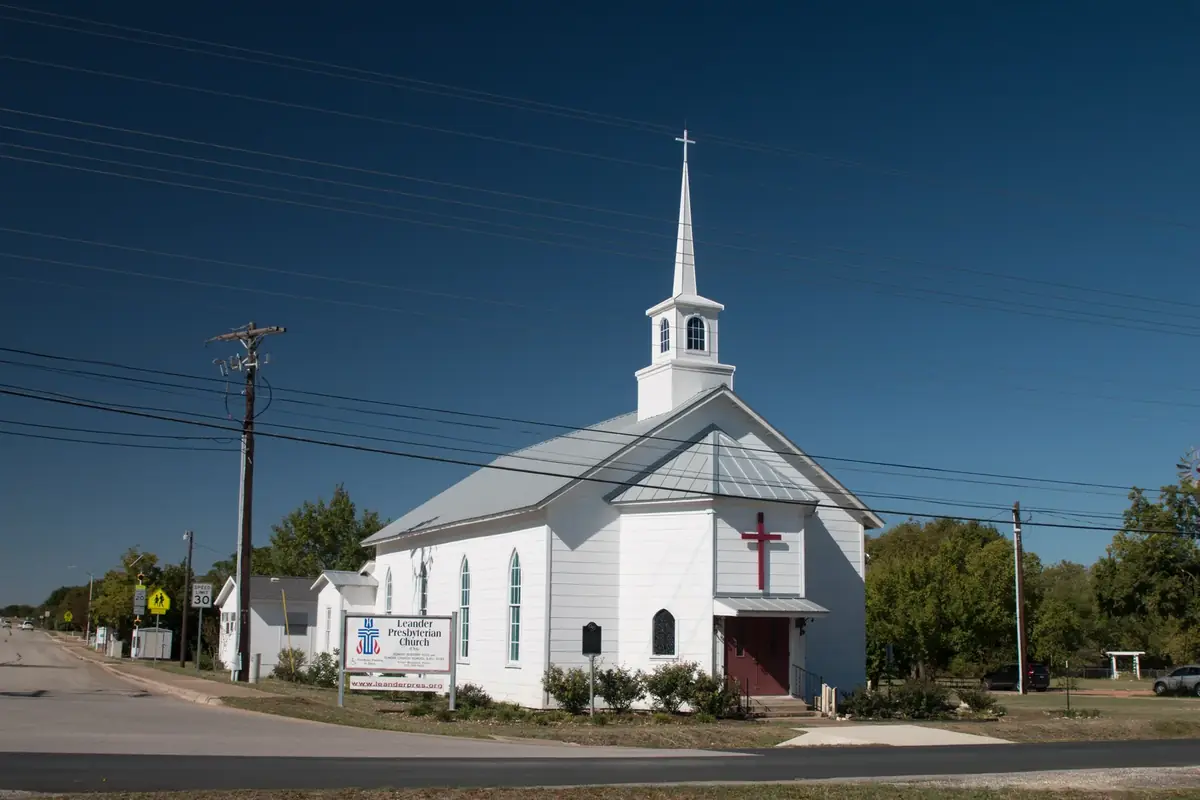 The white wooden Leander Presbyterian Church and its steeple under a deep blue sky