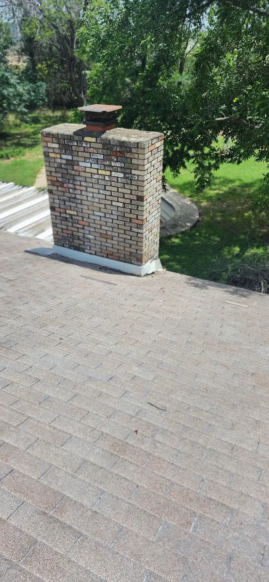 Finished roof at a brick chimney with clean new base flashing and a new chimney cap in full sun