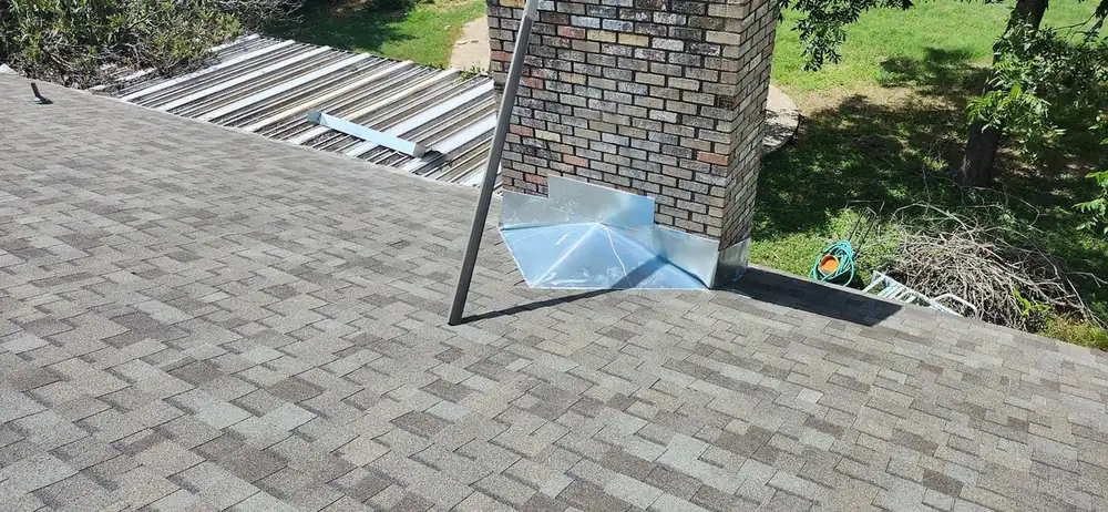 New dimensional shingles meeting a brick chimney with fresh galvanized step flashing and a saddle behind it