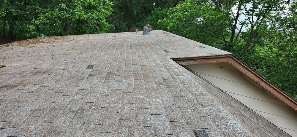 Worn tan roof looking up the slope to the ridge with a turbine vent, beside an open gable with exposed wood trim