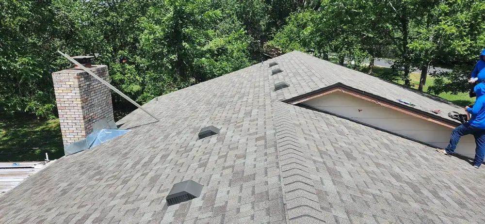 Finished architectural shingle roof with ridge caps, box vents and new chimney flashing seen along the ridge