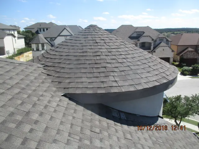 Completed shingle work wrapping a round turret roof above a neighborhood