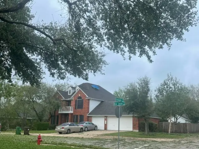 Two-story brick home with a tarped roof section on an overcast wet day