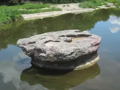 The table-shaped round rock sitting in the water of Brushy Creek