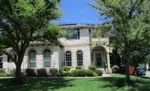 A two story limestone home behind live oaks, with a trimmed lawn in front